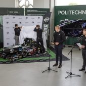 Dwóch mężczyzn odsłania nowy bolid, dwie osoby stoją przy mikrofonach