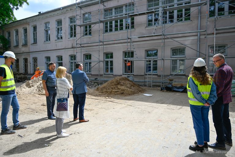 budowlańcy w kaskach przed zabytkowym gmachem szkoły