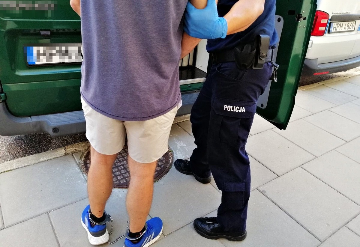 Policjant stoi przy skutym kajdankami mężczyźnie