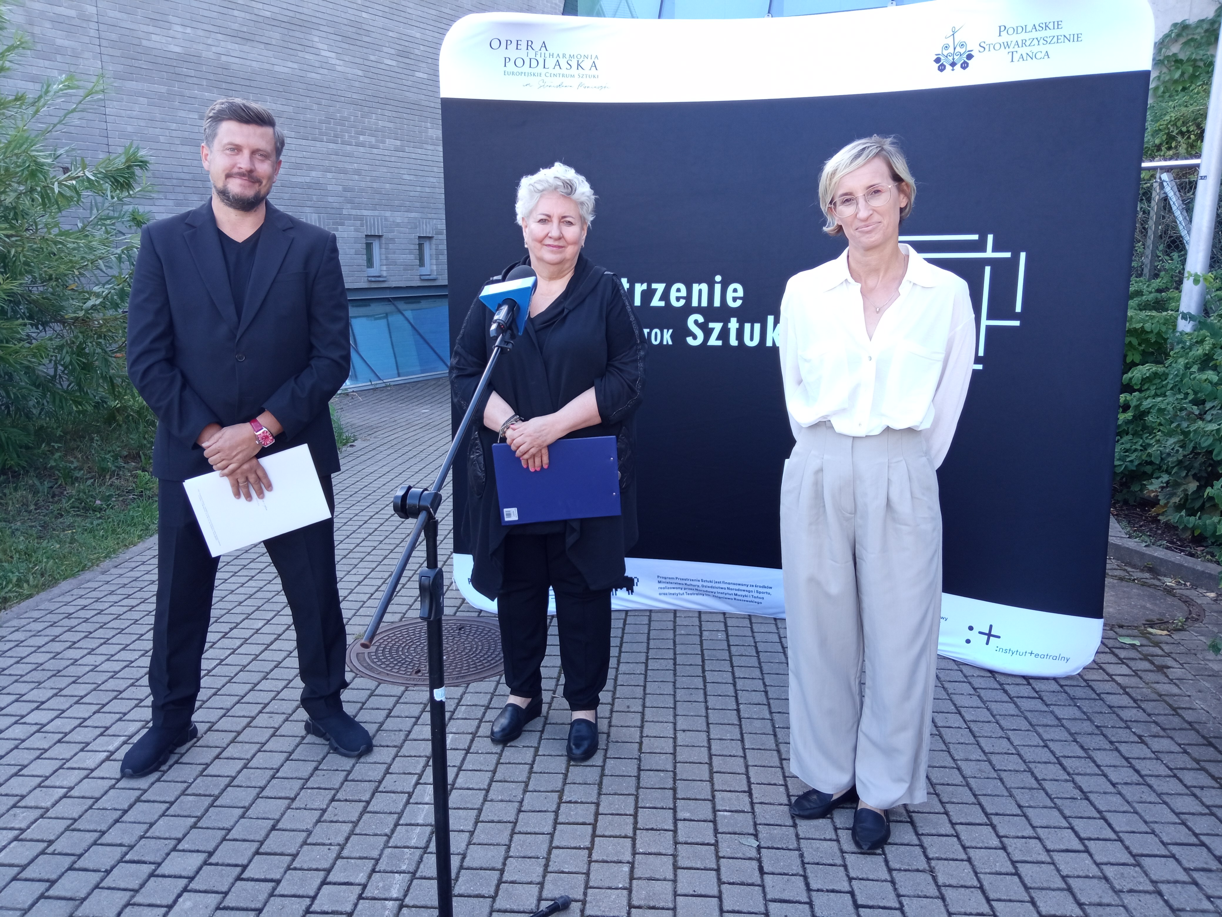 Diwe kobiety i mężczyzna stoją obok siebie na konferencji prasowej