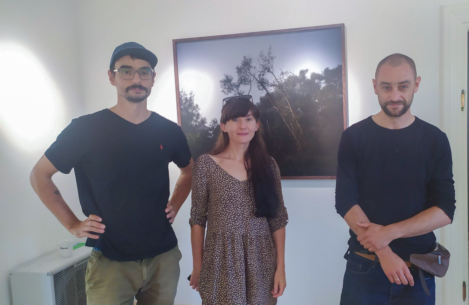 dwaj mężczyźni i kobieta stoją przed fotografią wiszącą na ścianie