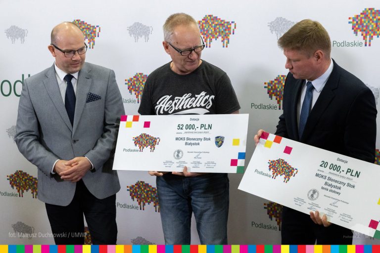 trzech mężczyzn, dwóch z nich trzyma symboliczne duże czeki