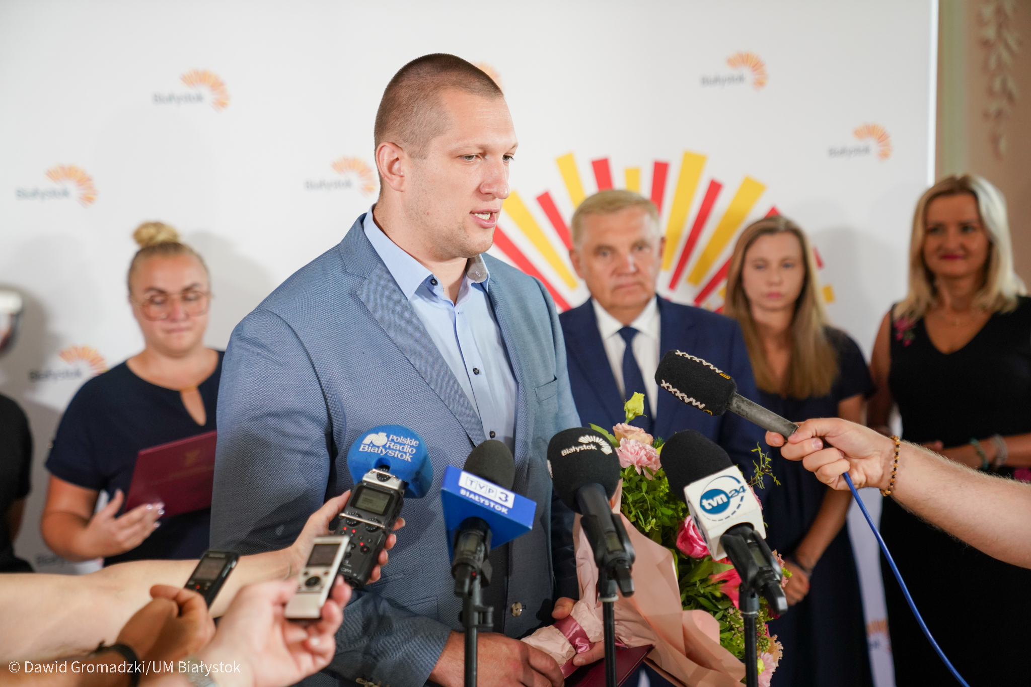 Wysoki mężczyzna mówi do mikrofonu dziennikarzy