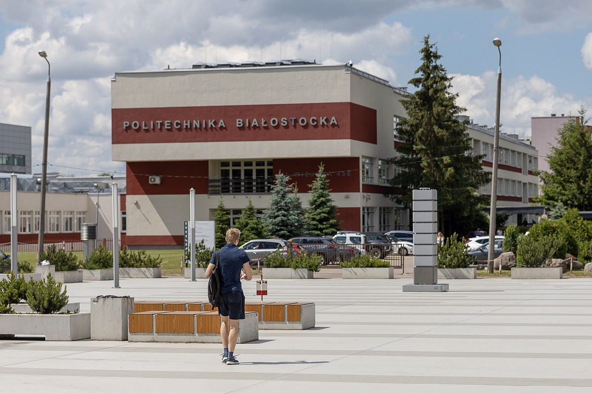 Budynek politechniki białostockiej, na placu przed budynkiem idzie młody mężczyzna