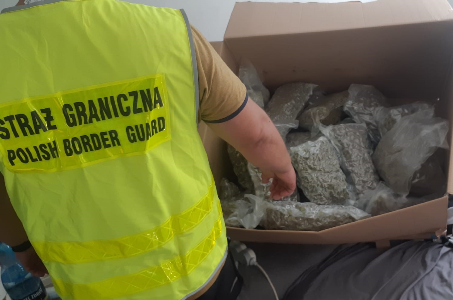 człowiek w kamizelce z napisem straż graniczna pokazuje ba pudełko z torebkami