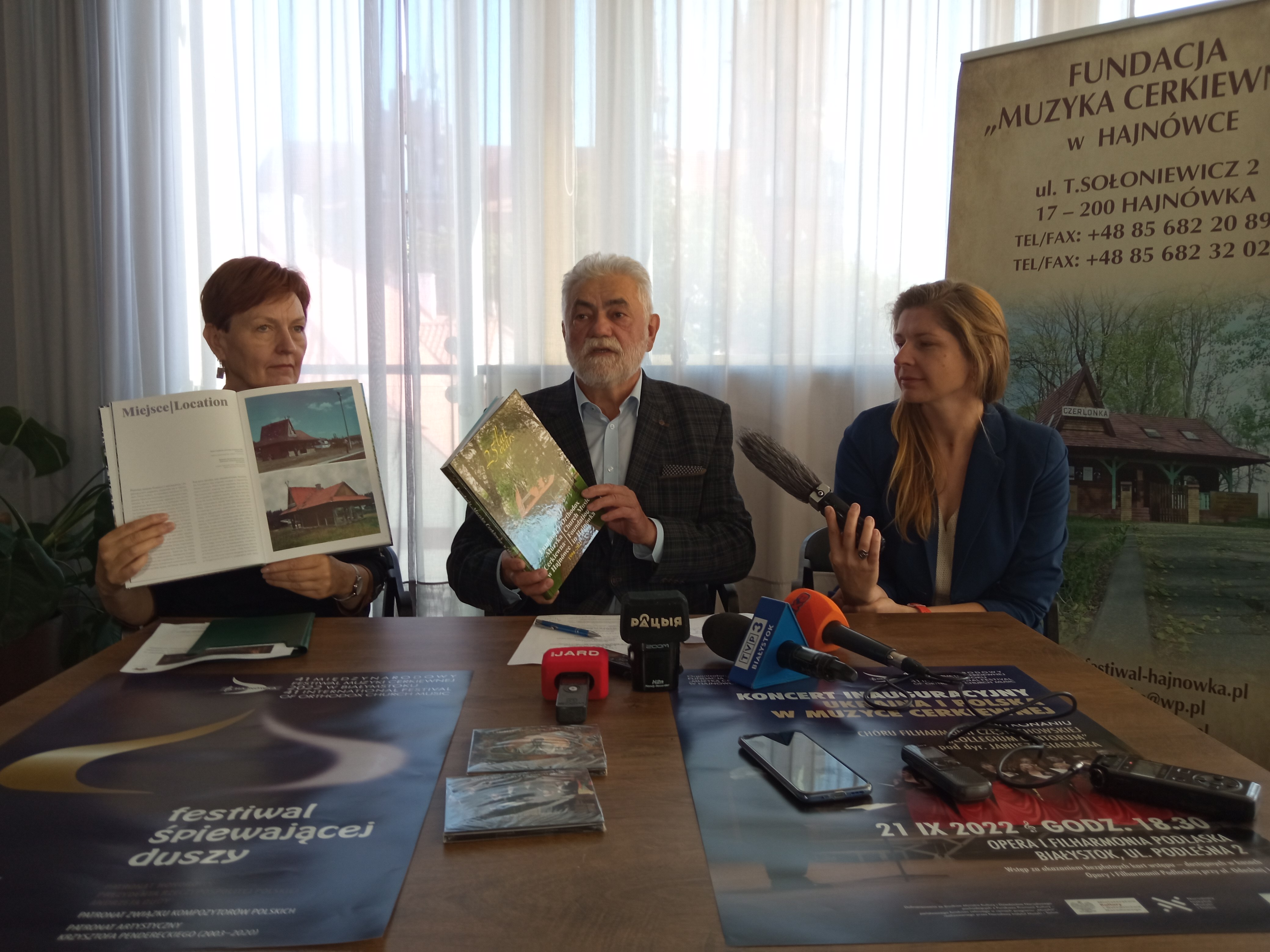 Trezy iosoby (dwie kobiety i mężczyzna prezentują album papierowy związany z festiwalem muzyki cerkiewnej