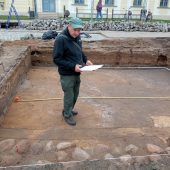 Mężczyzna stoi z papierowymi planami w wykopie archeologicznym