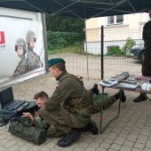 uczeń w mundurze leży na ziemi, obsługuje broń, obok instruuje go żołnierz
