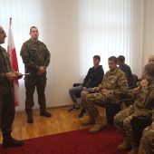Dwaj mężczyźni w mundurach stoją przed siedzącą młodzieżą w mundurach