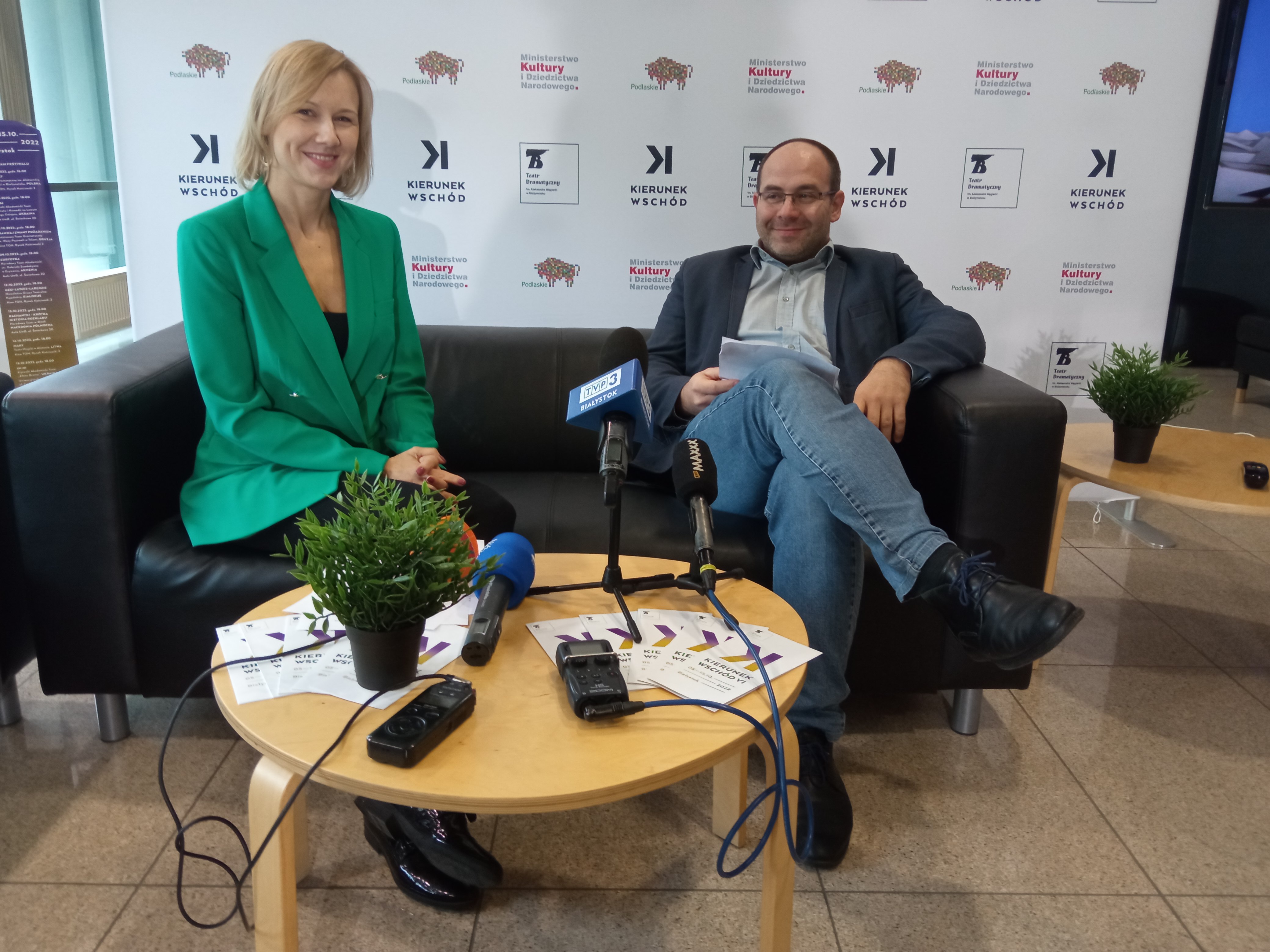 Na kanapie przy stoliku z mikrofonami siedzi kobieta i mężczyzna
