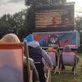 Ludzie siedzą na leżakach na trawie i oglądają film na ekranie na zewnątrz