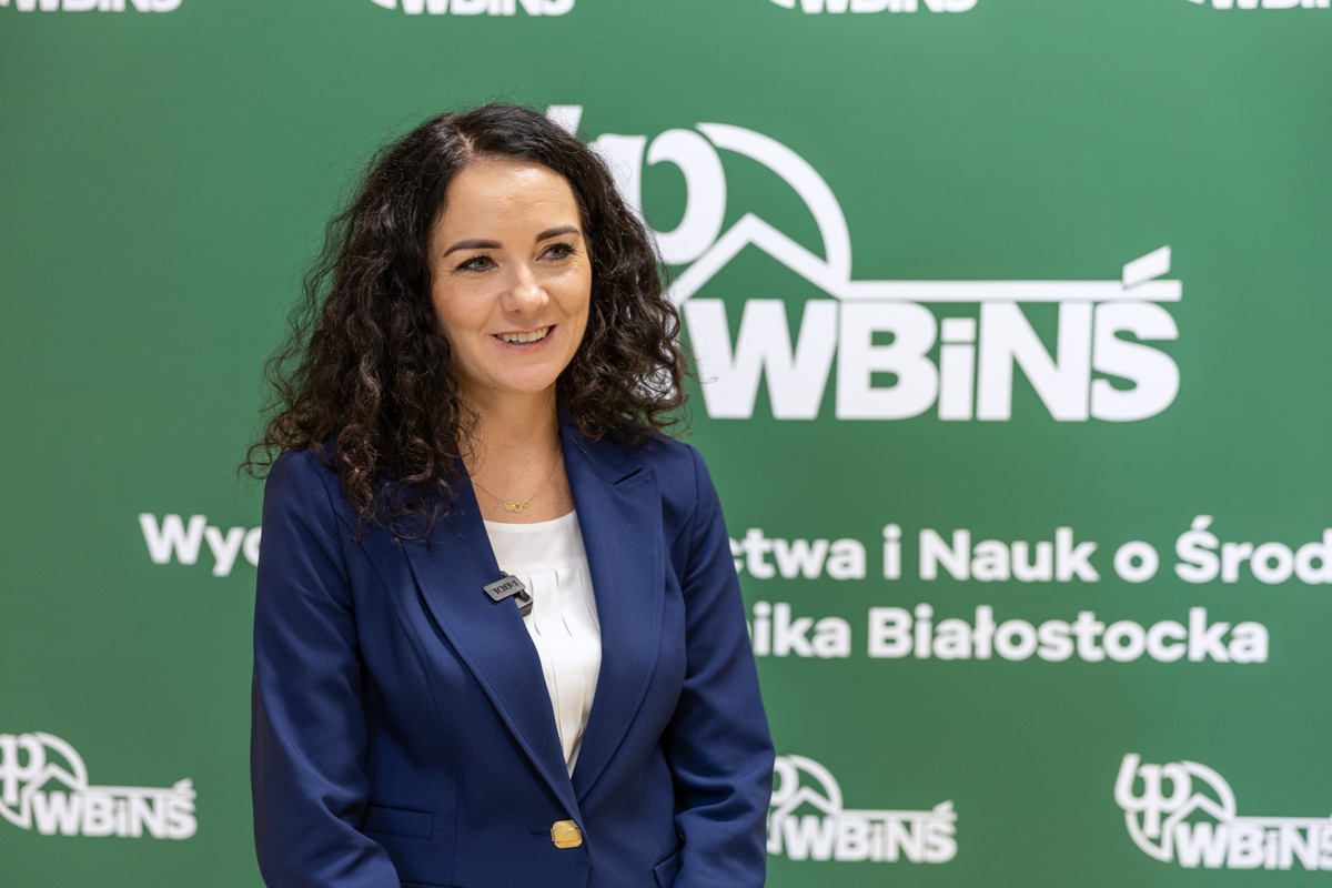 Uśmiechnięta kobieta w eleganckiej marynarce na tle banera