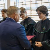 Mężzyzna w garniturze ściska dłoń ucznia. Obok stoją inni uczniowie