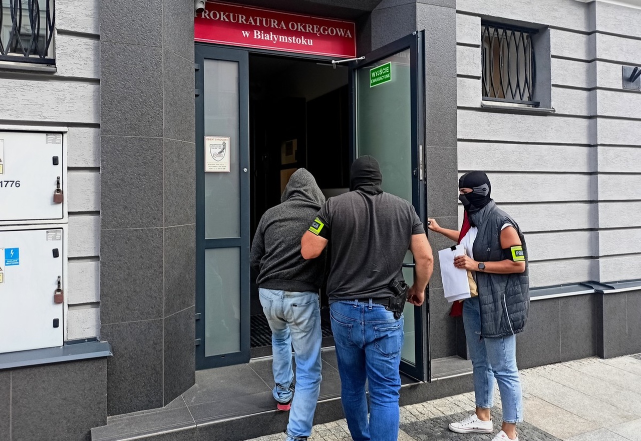 policjanci wprowadzający zatrzymanego do budynku