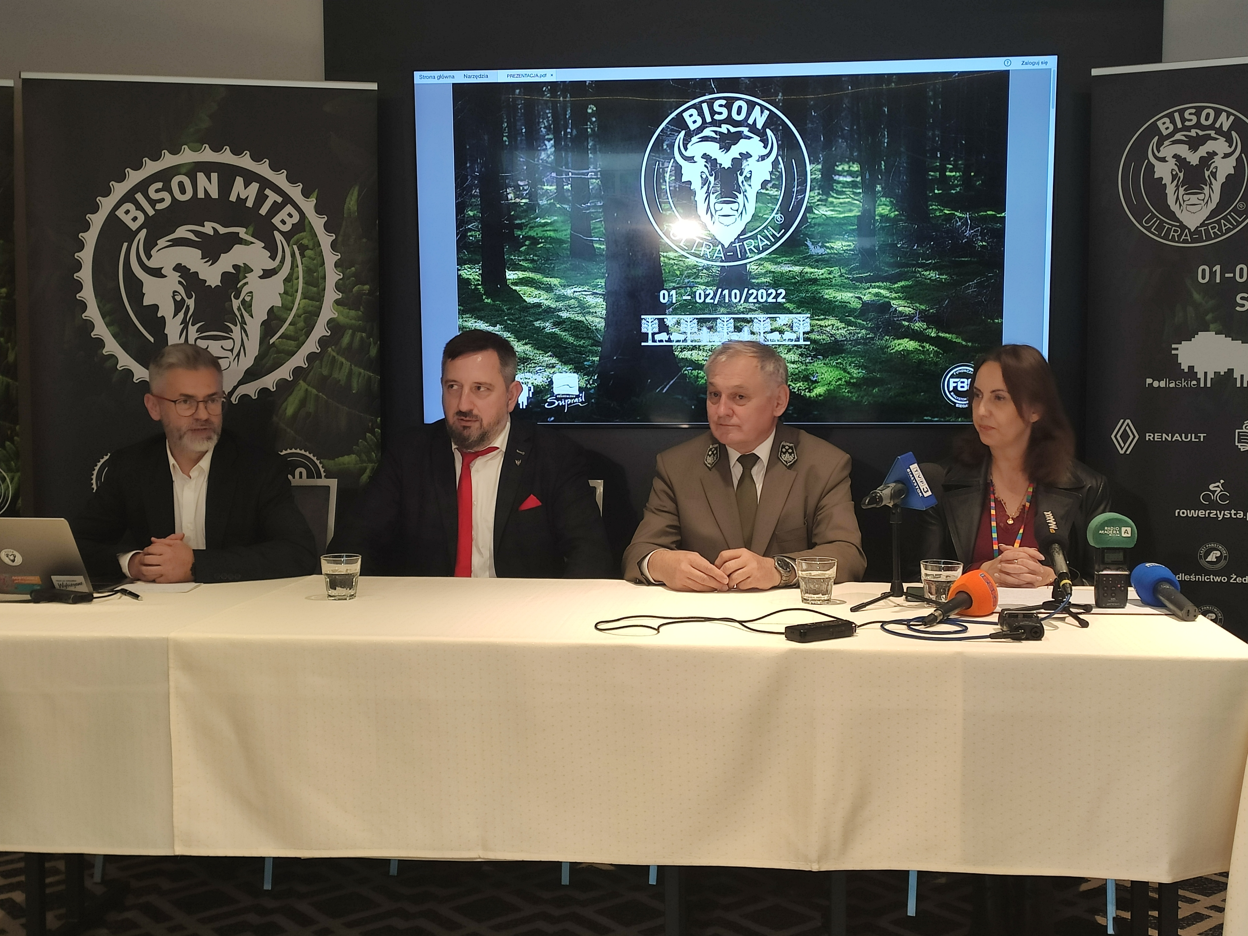 Cztery osoby siedzą za stołem, na którym stoją mikrofony