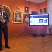 Mężczyzna stoi na tle portretó Branickich, obok na telebimie wyświetla się nowa strona internetowa
