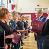 Mężczyzna wręcza nagrody i gratuluje kobiecie. Obok stoją inne wyróżnione panie