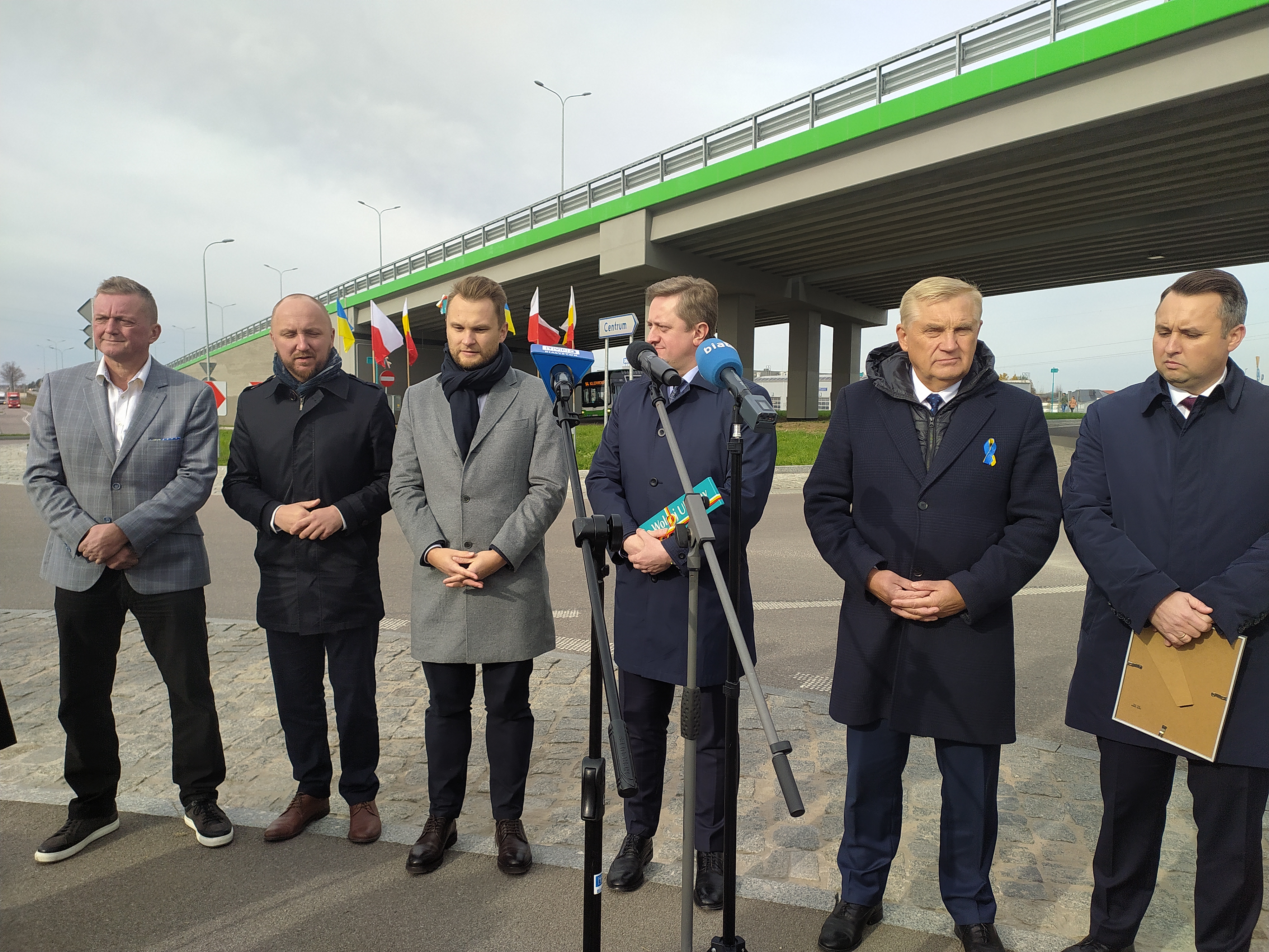 Sześcioro mężczyzn stoi na chodniku przy wiadukcie obok ronda