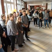 Grupa studentów stoi w hlou i słucha wystąpień