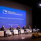Na scenie na fotelach siedzi sześć osób, za nimi wyśietla się napis Podlaskie Forum Ekonomiczne