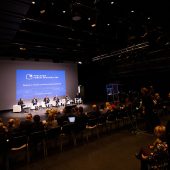 Na scenie w fotelach siedzi sześć osób, widownia jest pełna