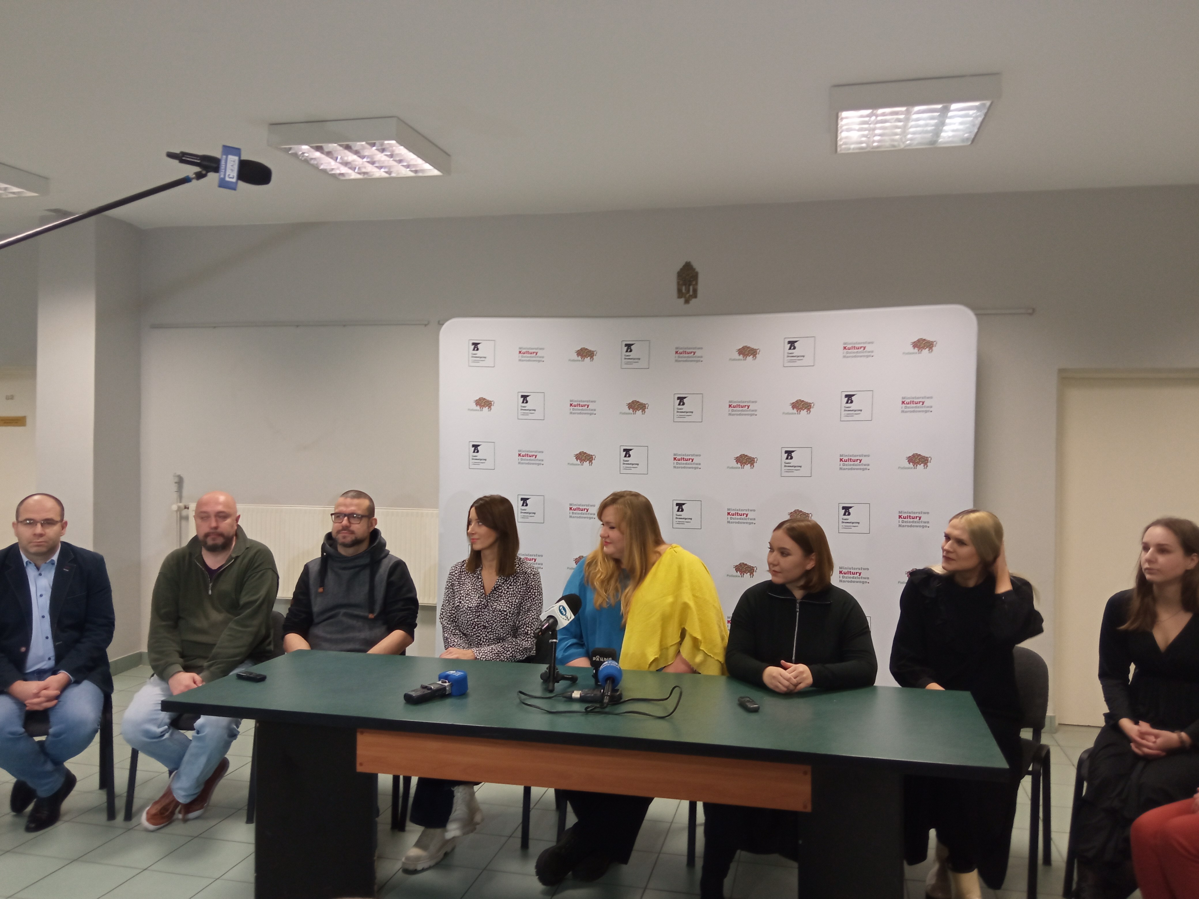 Za stołem siedzi osiem osób, aktorki, reżyserka, autor muzyki, scenograf, dyrektor teatru