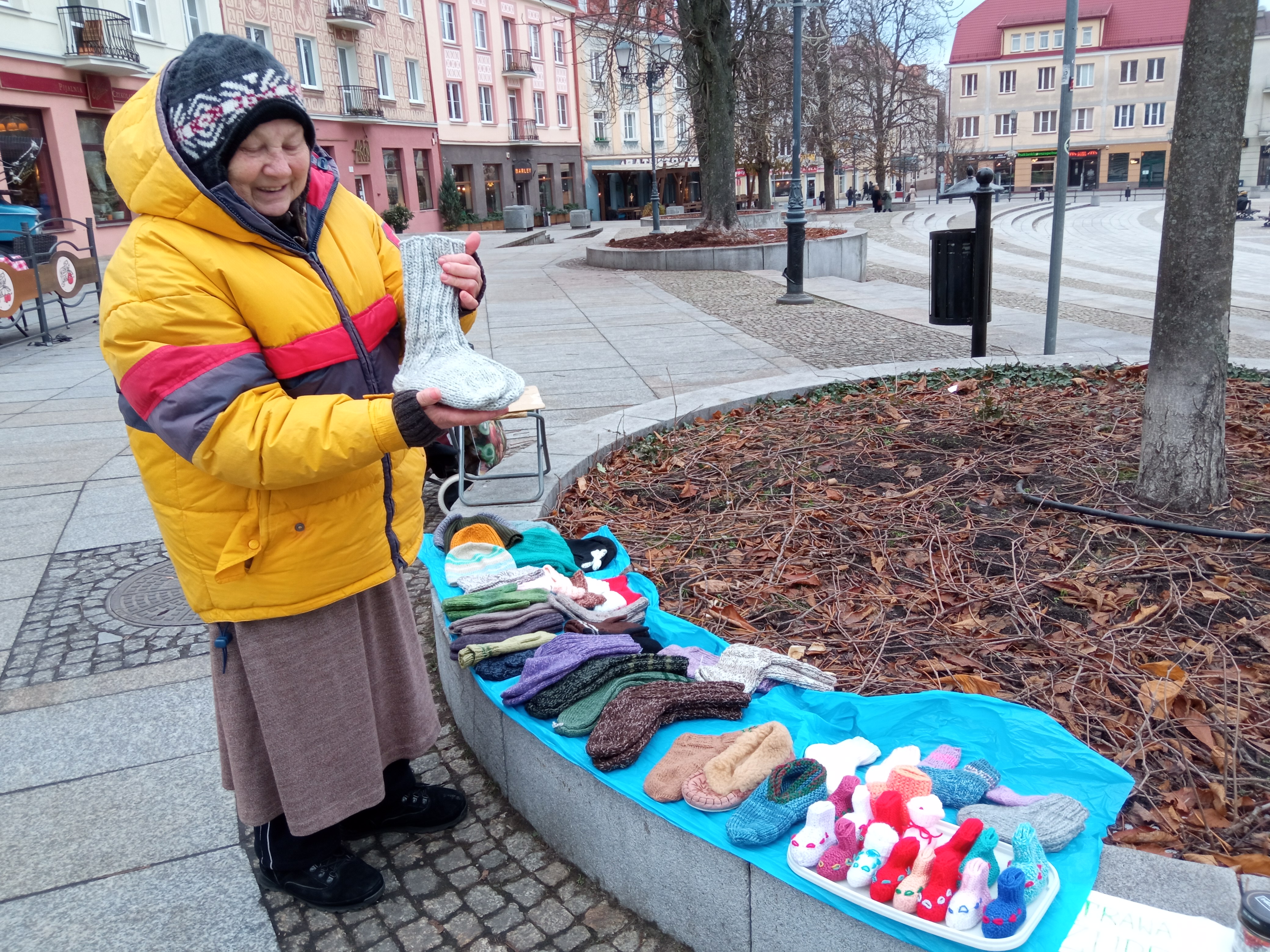 Starsza pani trzyma własnoręcznie zrobione ciepłe skarpety, obok leży kilka innych par