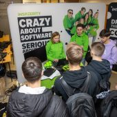 Grupa młodych ludzi stoi przy stoisku wystawienniczym firmy