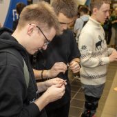 Młodzi ludzie stoją przy stoisku wystawienniczym firmy, trzymają gadżety