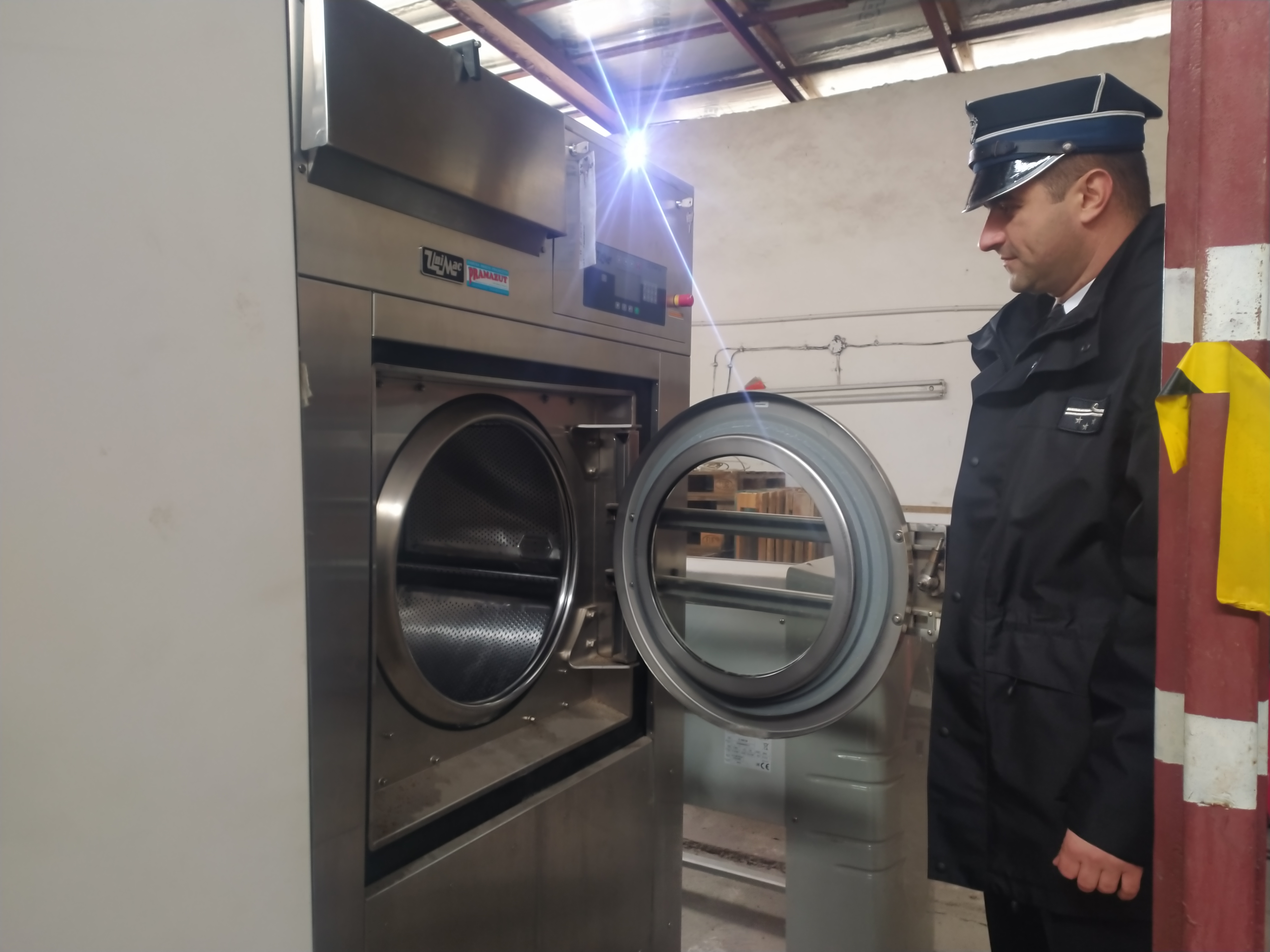 Strażak OSP w służbowym graniturze stoi przed przemysłową pralnicą