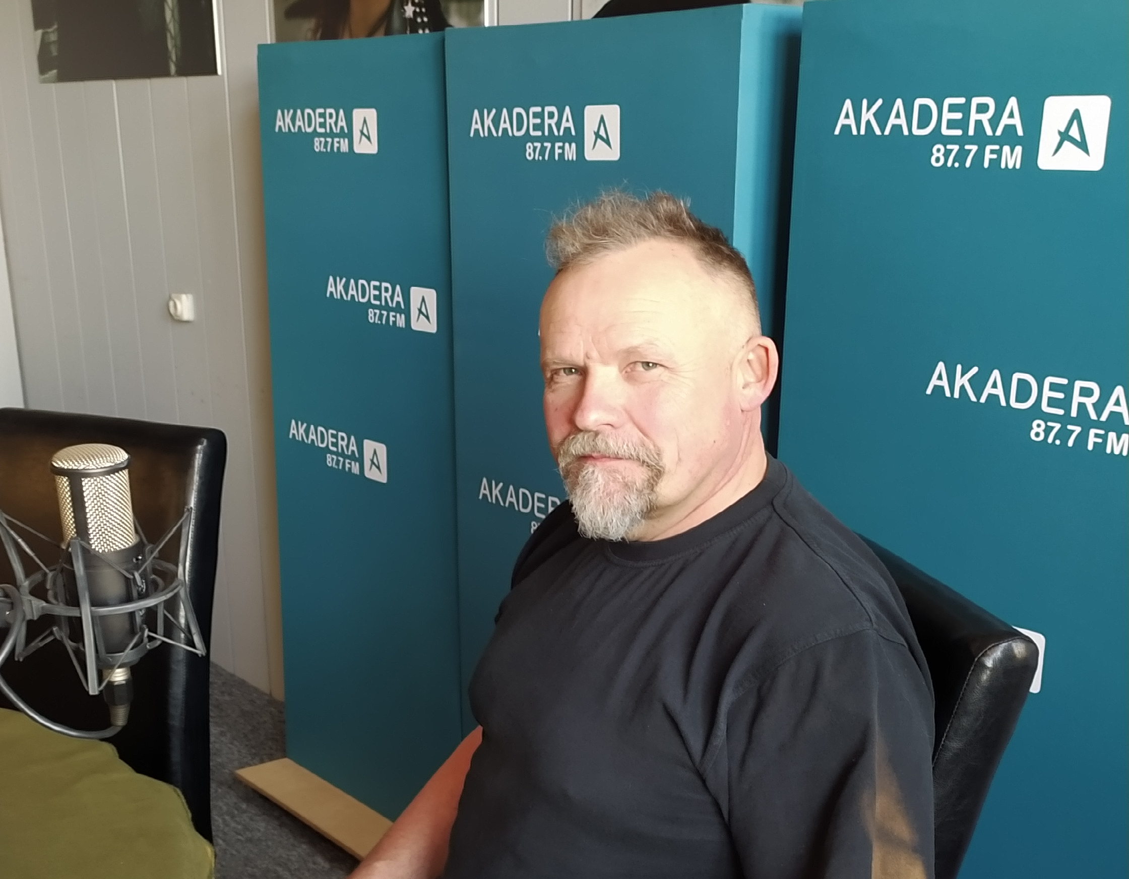 Siwy mężczyzna w średnim wieku siedzi w studio radiowym przed mikrofonem