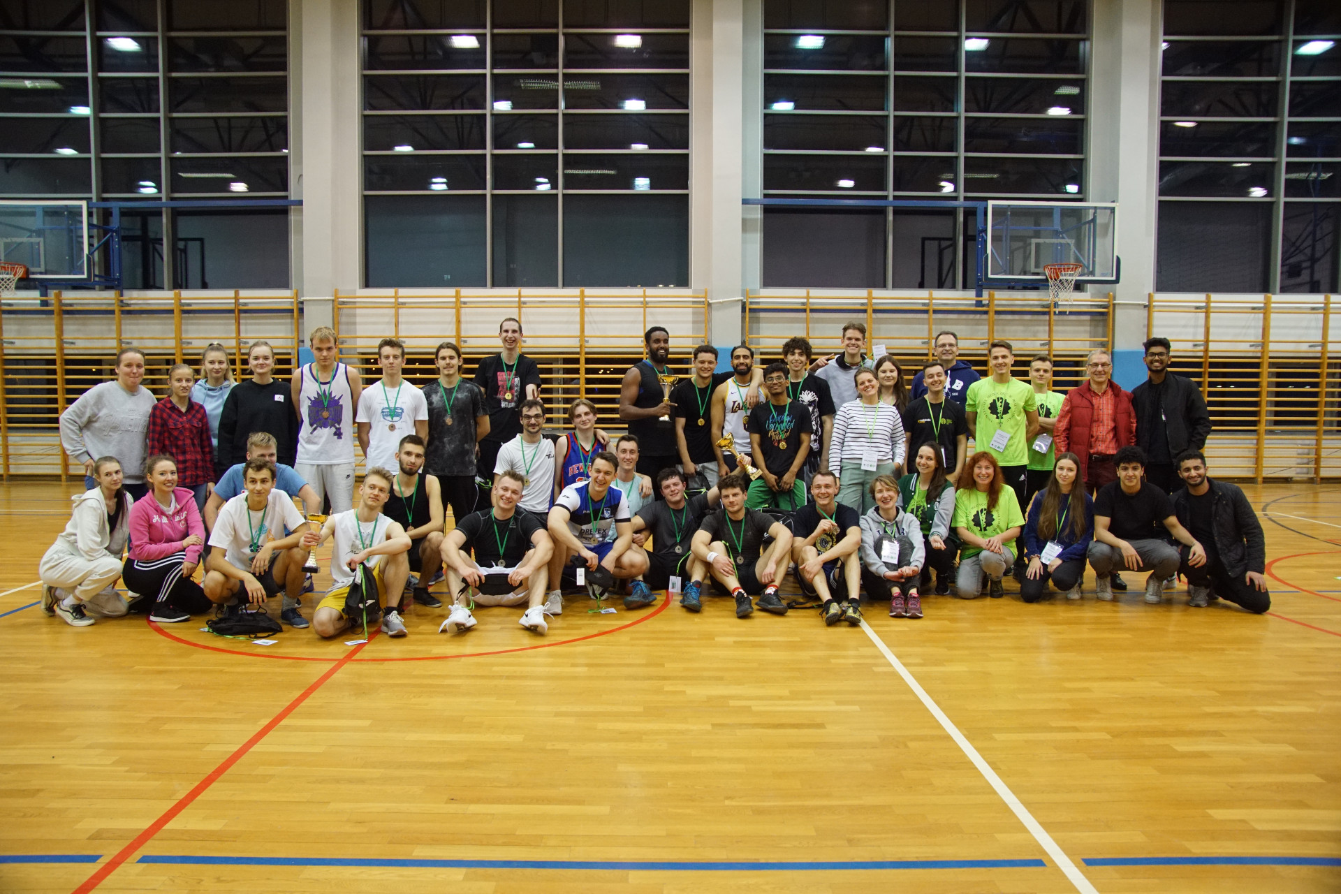 Kilkadziesiąt osób w sportowych ubraniach pozuje do zdjęcia na hali sportowej