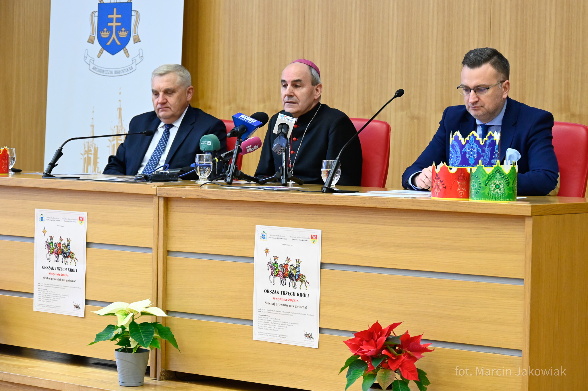 Trzech mężczyzn siedzi za stołem, przed nimi stoją mikrofony.
