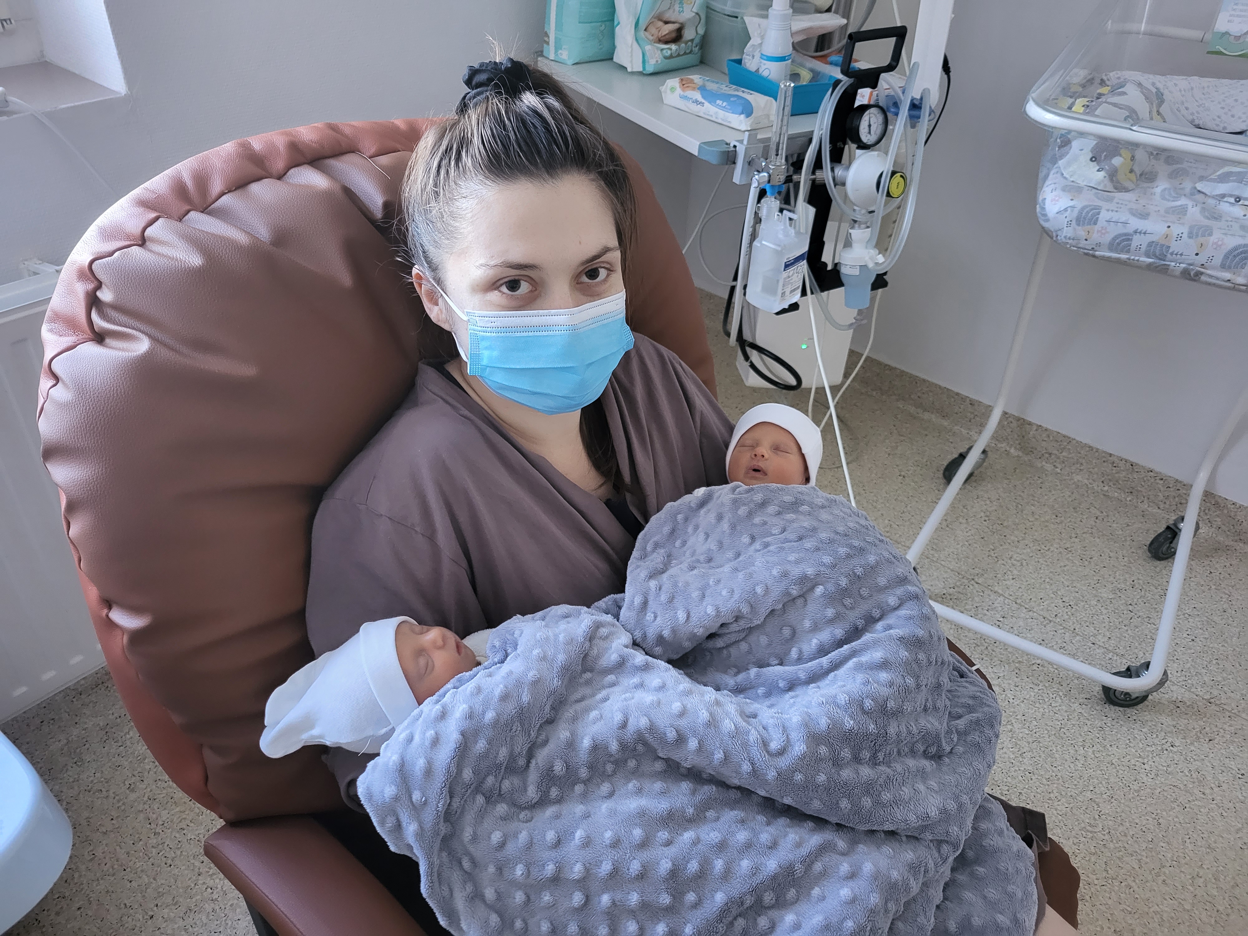 Mam siedzi i trzyma na rękach dwoje dzieci - noworodki