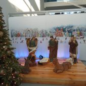 Obok dużej choinki na podeście figurki Maryi, żłóbek,pastuszkowie i zwierzeta, w tle grafika miasta