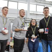 Cztery osoby tzrymają na dłoni miniaturowy fragment ceglanego muru