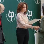 Kobieta gratuluje studentce i wręcza nagrode; obok stoi uśmiechnięty mężczyzna