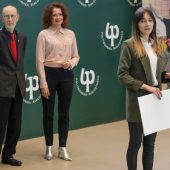 Młoda kobieta mói do mikrofonów, z tyłu stoi mężczyzna i kobieta