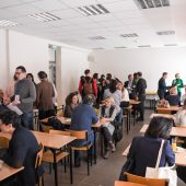 Grupa osób rozmwia ze sobą przy stolikach na sali