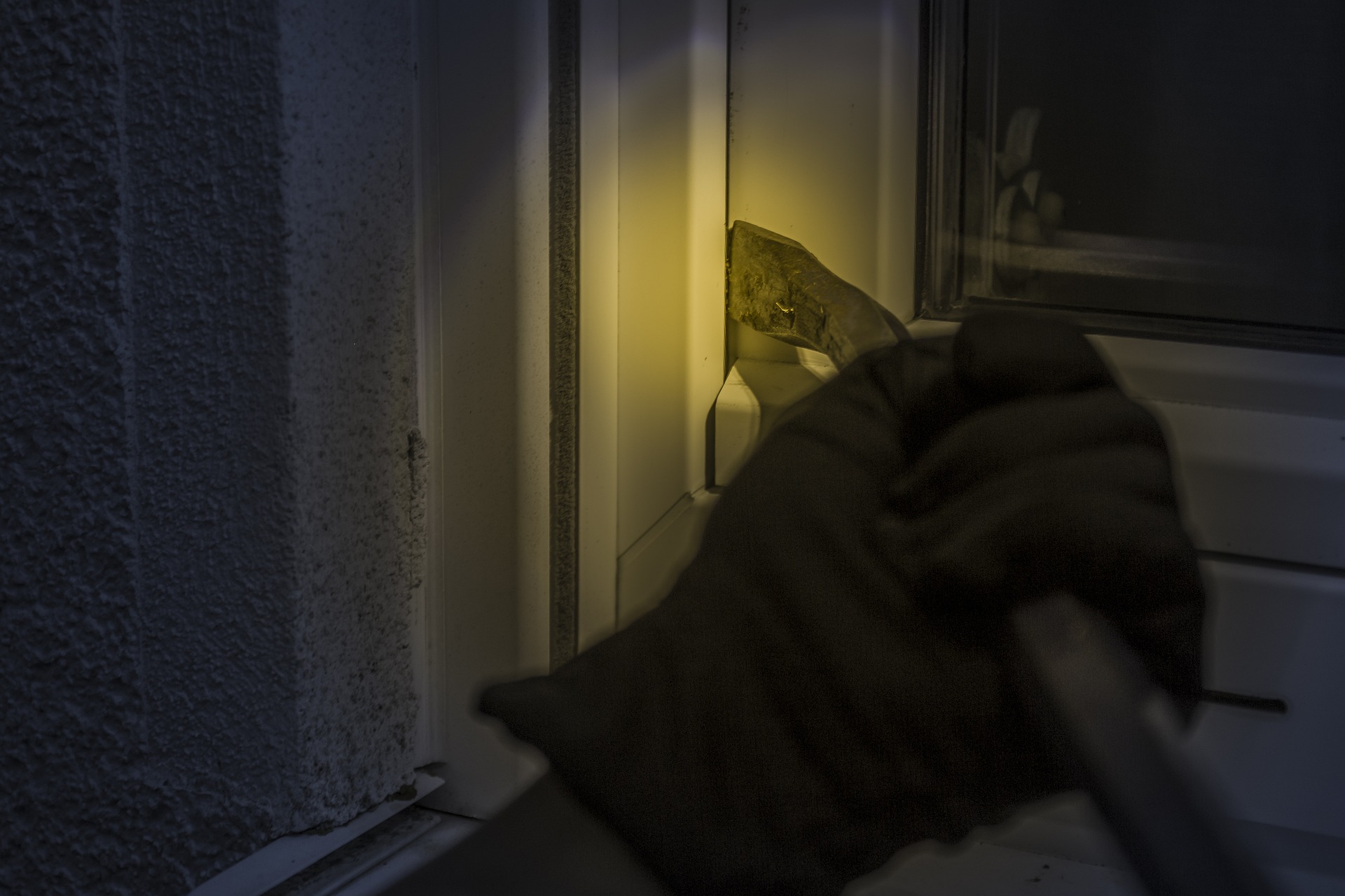 Dlon w rękawicze trzyma łom i podważa okno