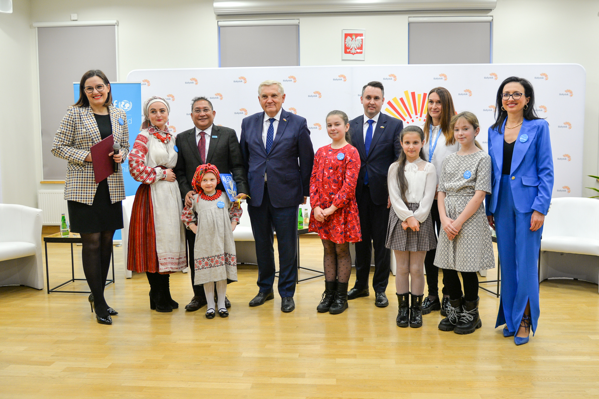 Kilka osób dorosłych i cztery dziewczynki pozuje do zdjęcia , dwie osoby są w strojach ludowych.