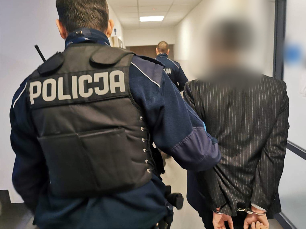 Policjant prowadzi skutego kajdankami mężczyznę