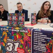 Trzy osoby siedzą za stołem, przed nimi stoją puszki WOŚP 2023 i plakaty