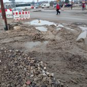 Dziury i błoto na przebudowywanych chodnikach, obok ida piesi