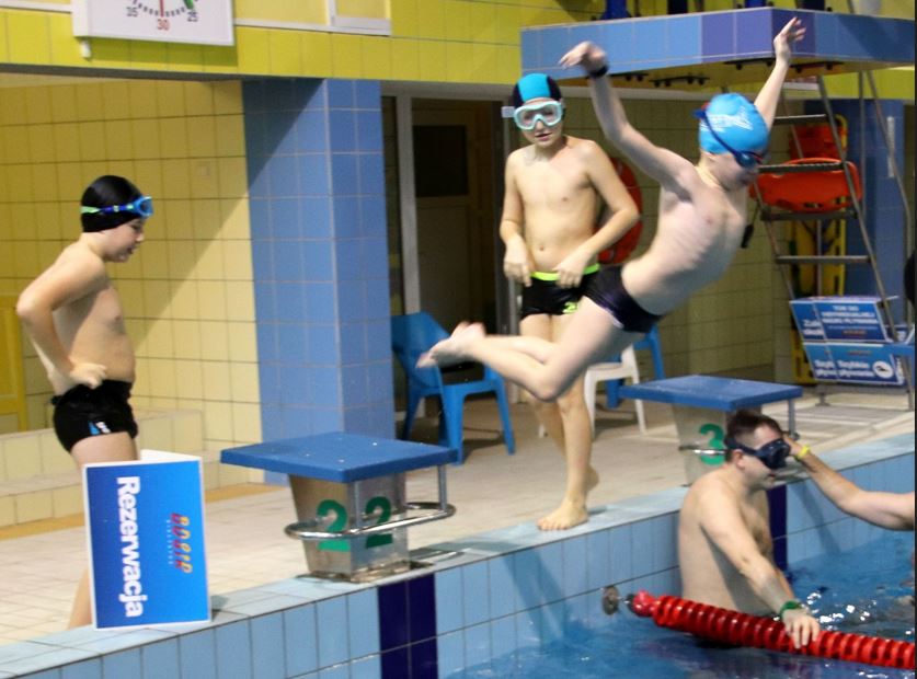 Dzieci w czepkach skaczą dow wody na basenie