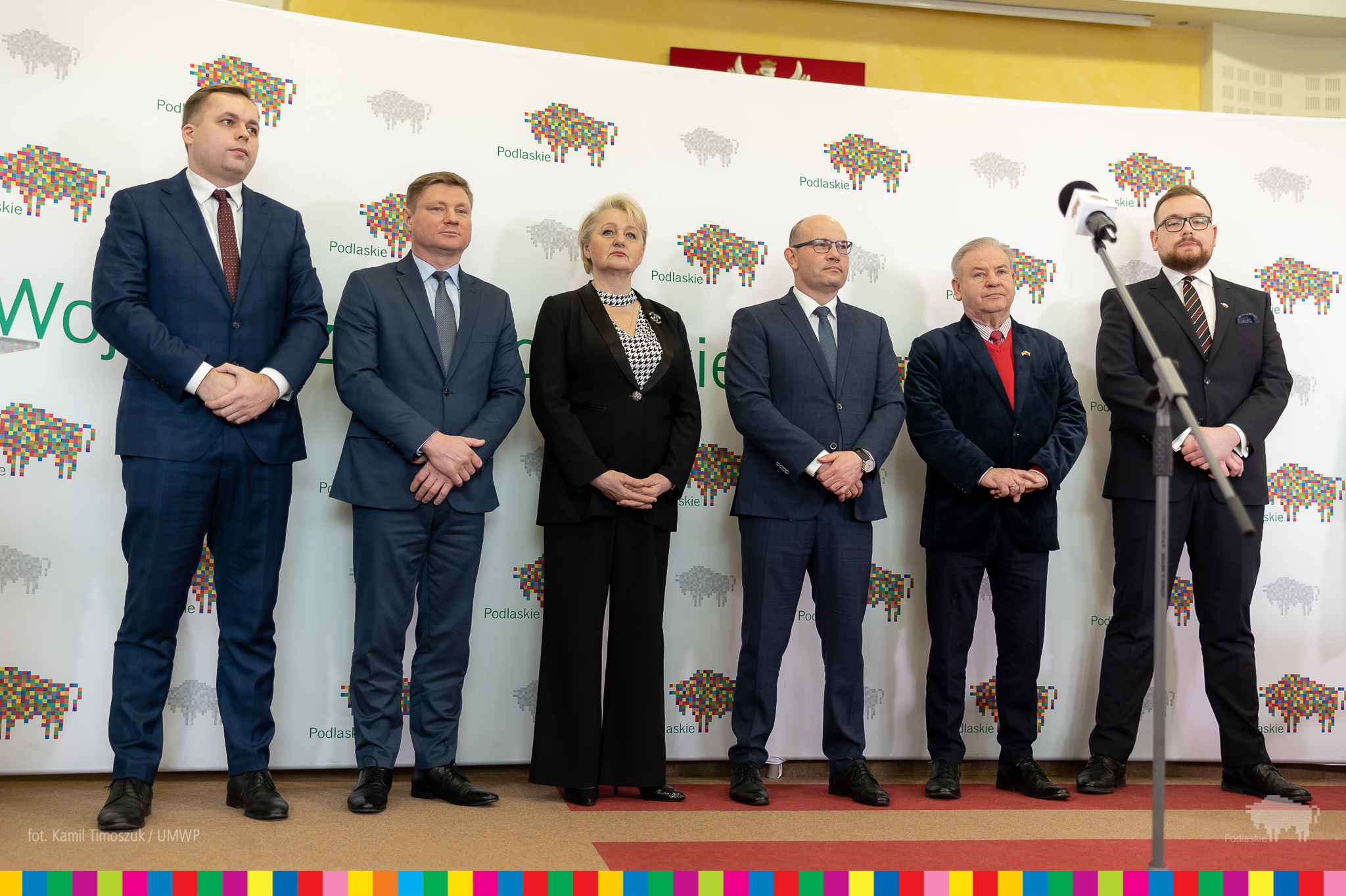 Sześć osób w garniturach pozuje do zdjęcia na tle baneru województwa podlaskiego.