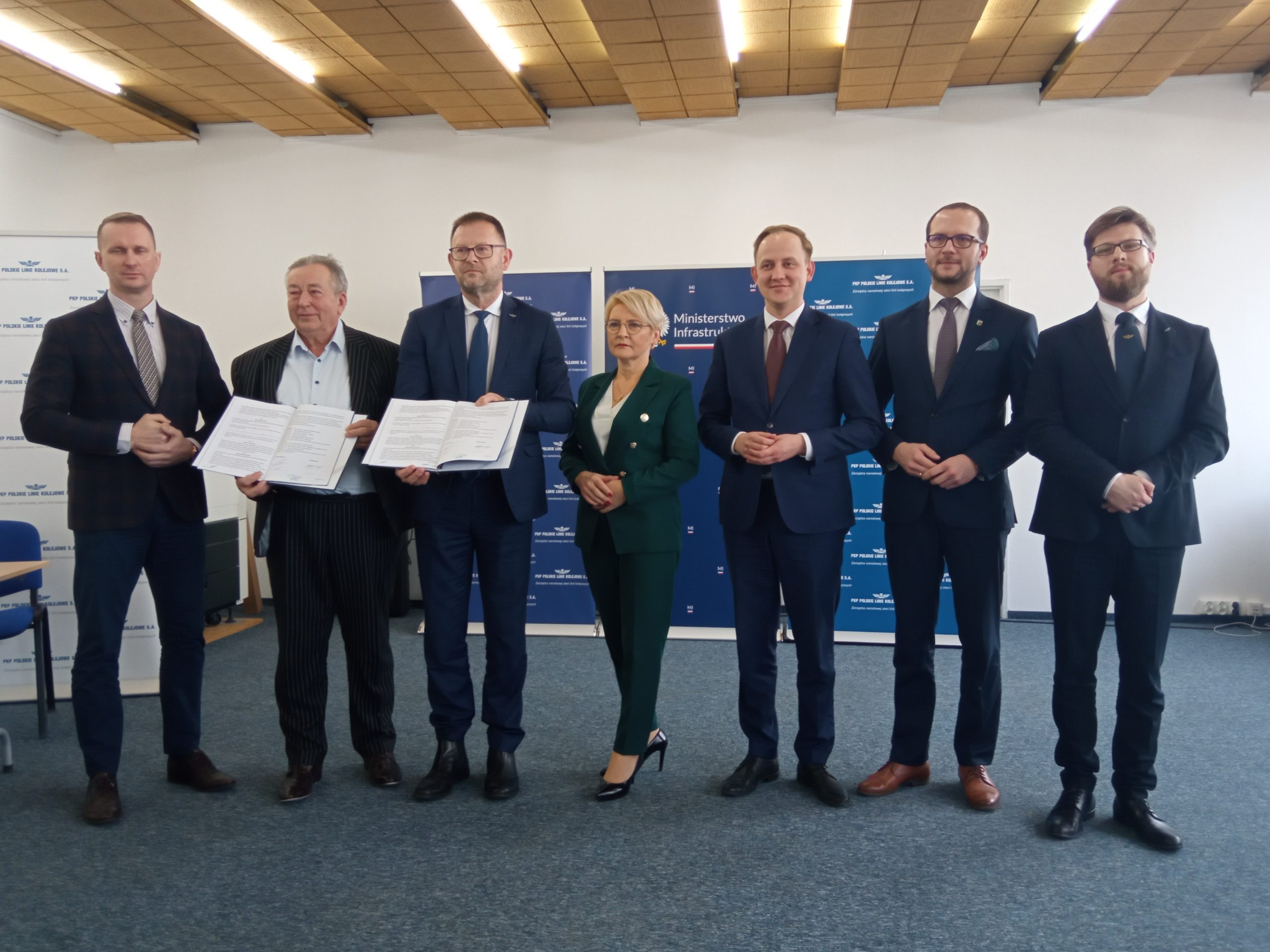 Grupa osób stoi, trzymają podpisane dokumenty