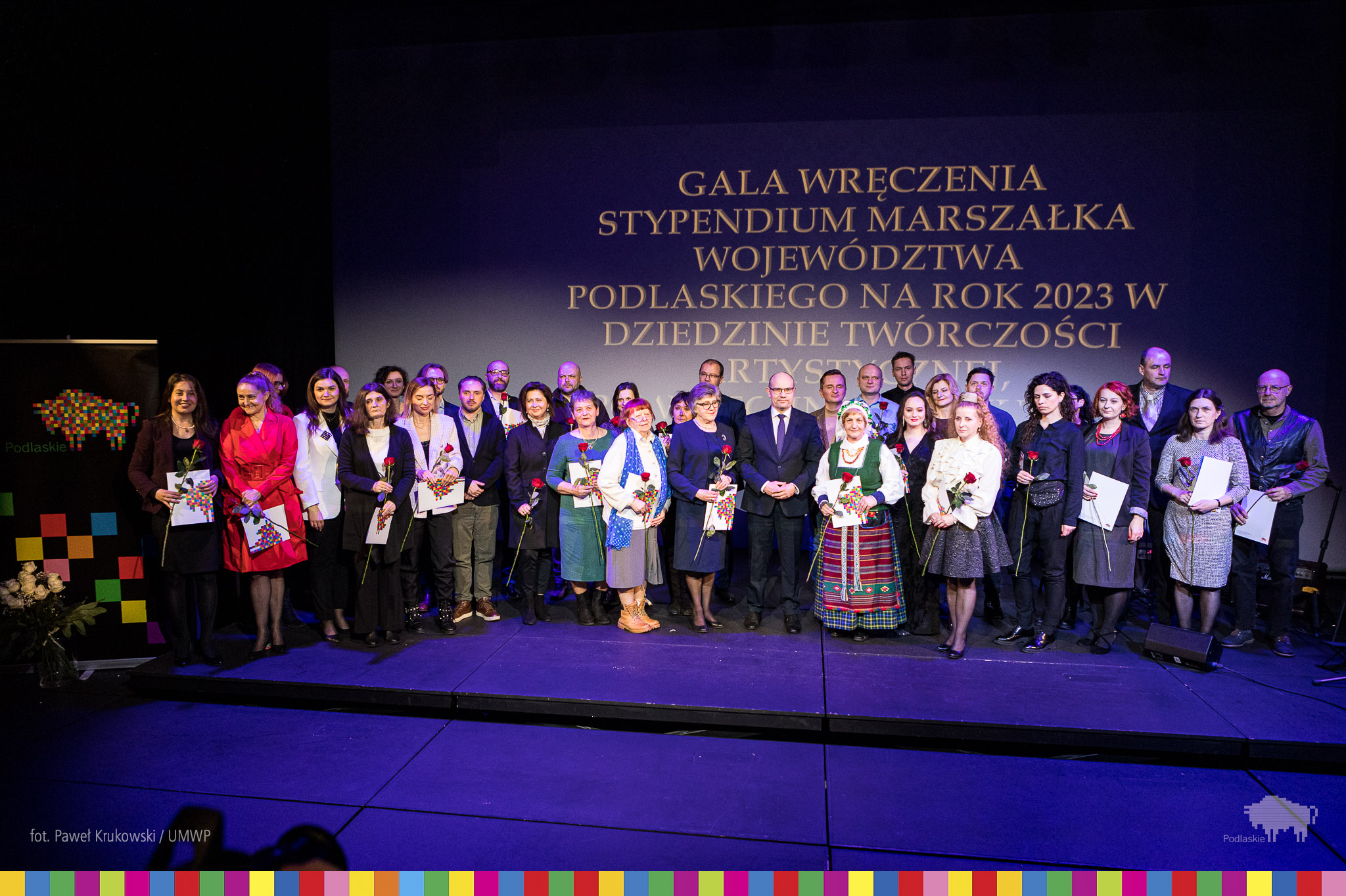 Grupa osób z kwiatami i wyróżnieniami stoi na scenie