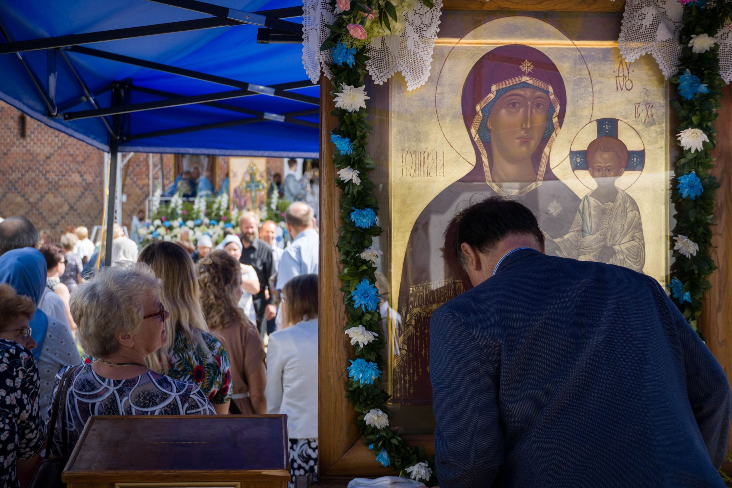 Mężczyzna dotyka czołem ikony Matki Boskiej, obo stoją wierni