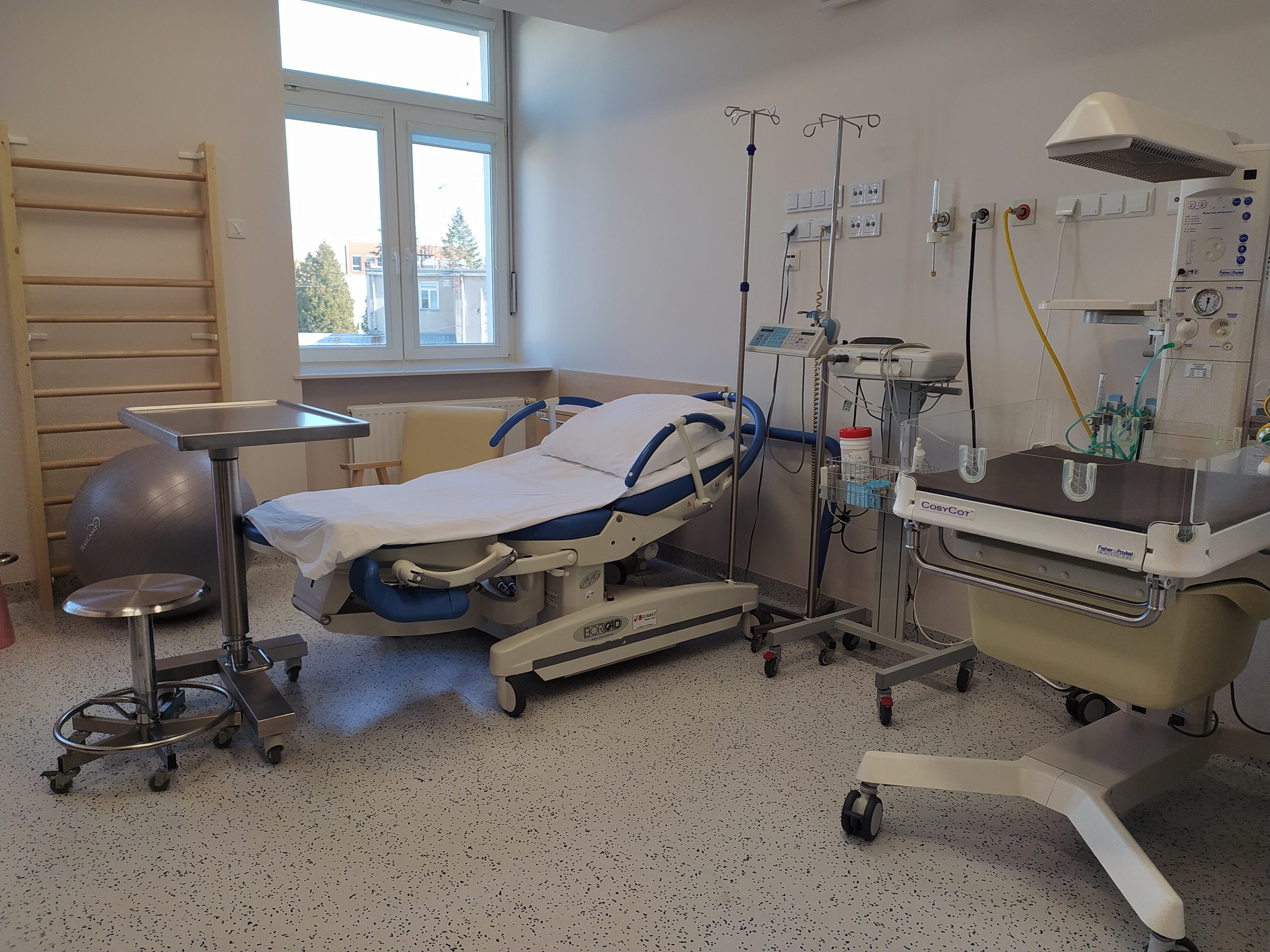 Sala porodowa, w której stoi łóżko do porodu, miejsce dla dziecka i aparatura medyczna.